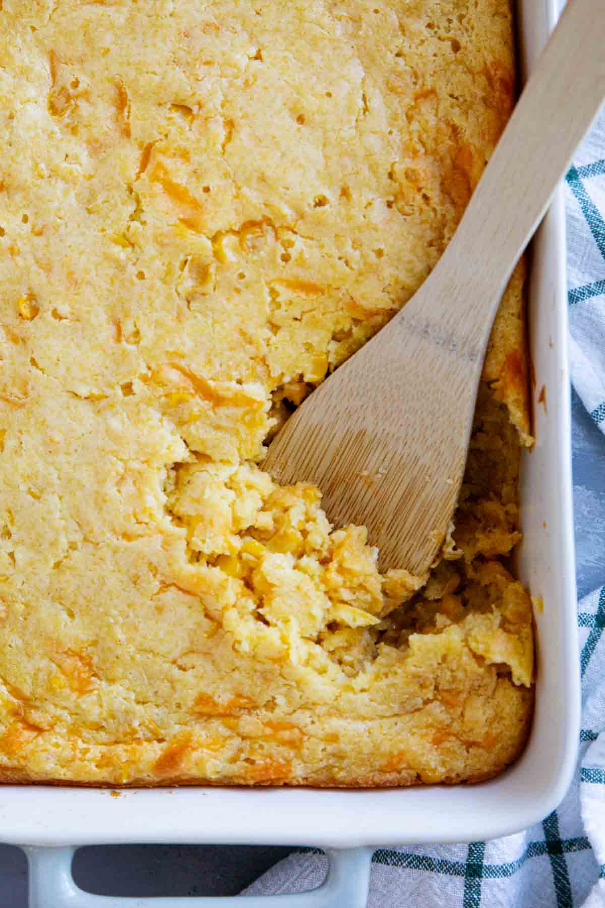 Dish of corn casserole with a wooden spoon.