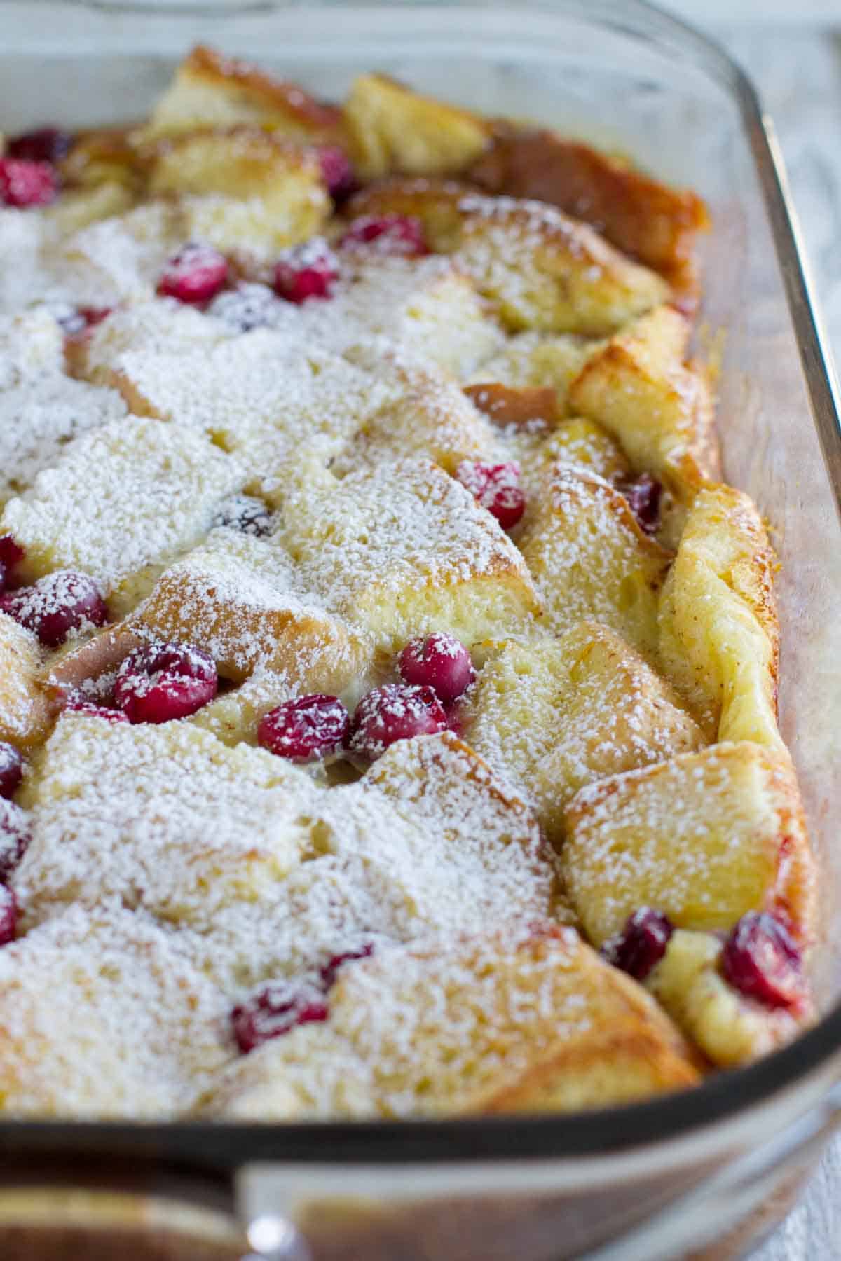 Cranberry orange baked French toast casserole in a baking dish topped with powdered sugar.