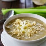 Bowl of green chicken enchilada soup topped with cheese and crushed tortilla chips.