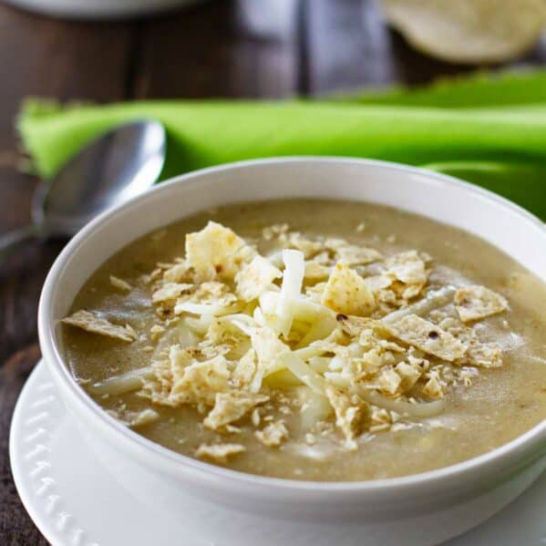 Bowl of green chicken enchilada soup topped with cheese and crushed tortilla chips.