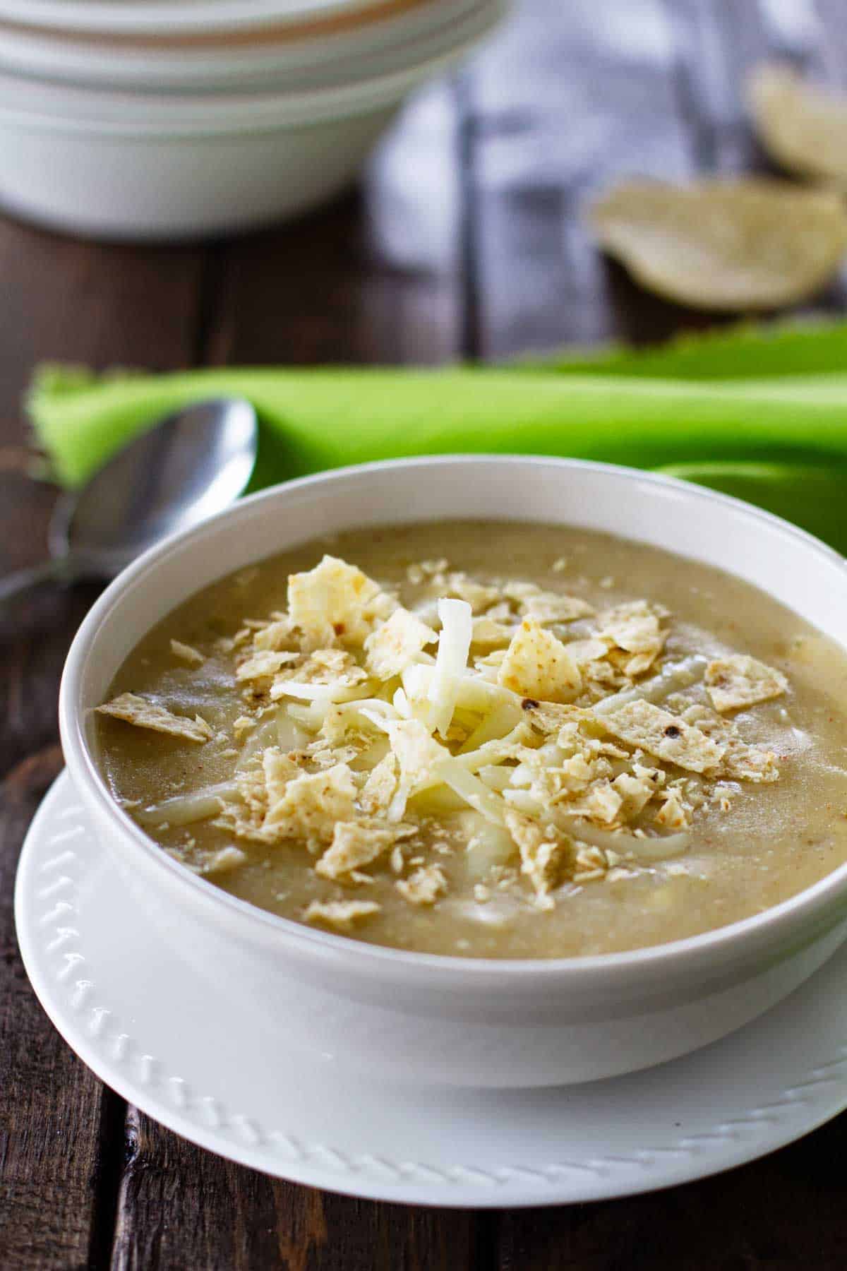 Bowl of green chicken enchilada soup topped with cheese and crushed tortilla chips.