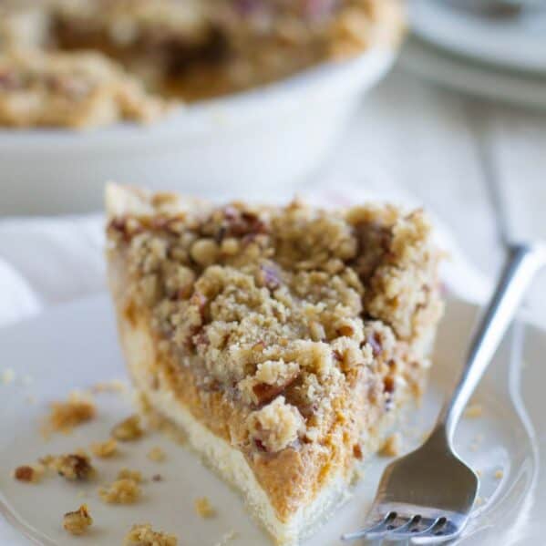Single slice of pie with layers of cheesecake and pumpkin pie with a streusel topping.