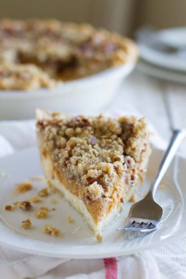 Single slice of pie with layers of cheesecake and pumpkin pie with a streusel topping.