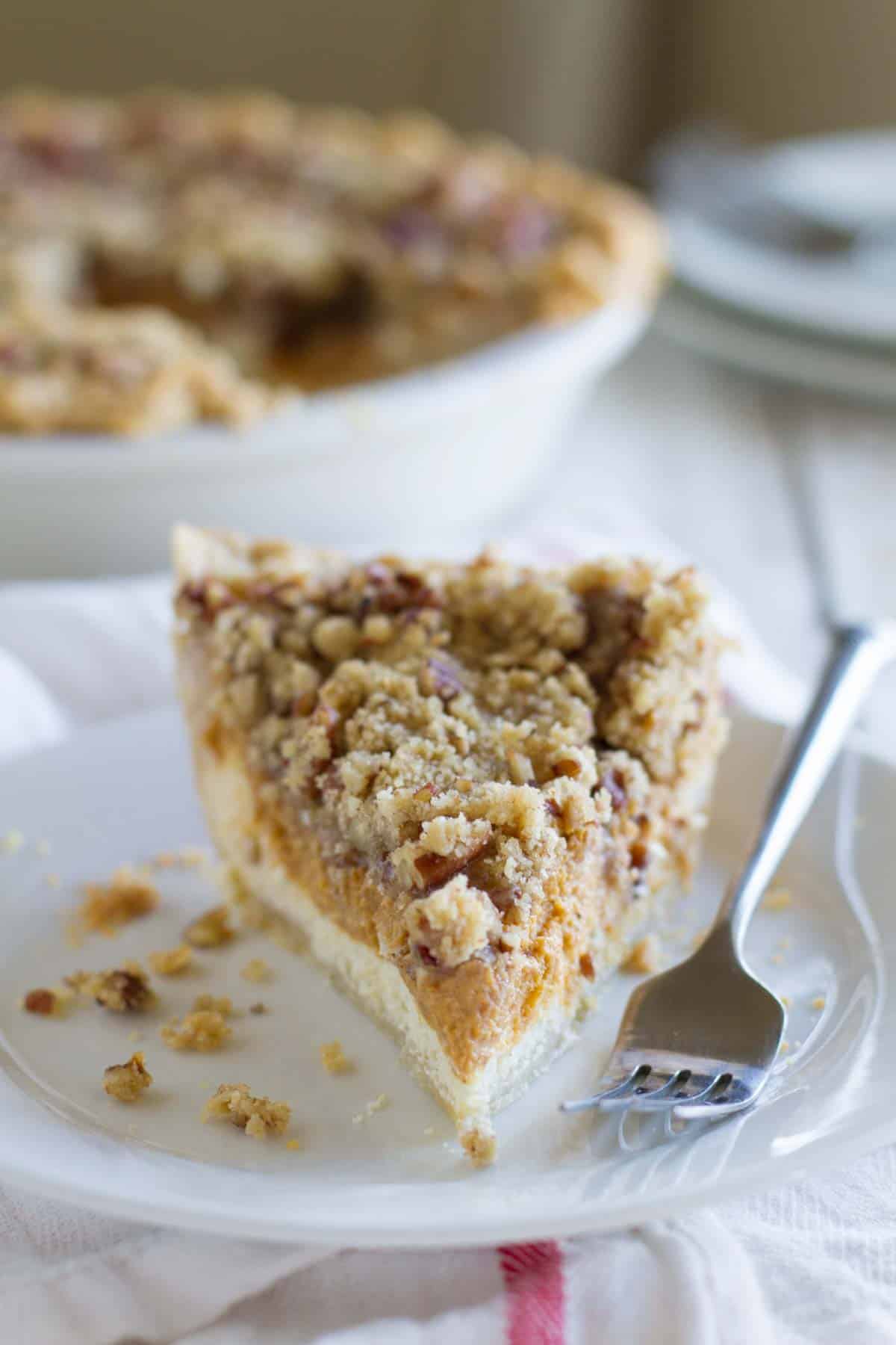 Single slice of pie with layers of cheesecake and pumpkin pie with a streusel topping.