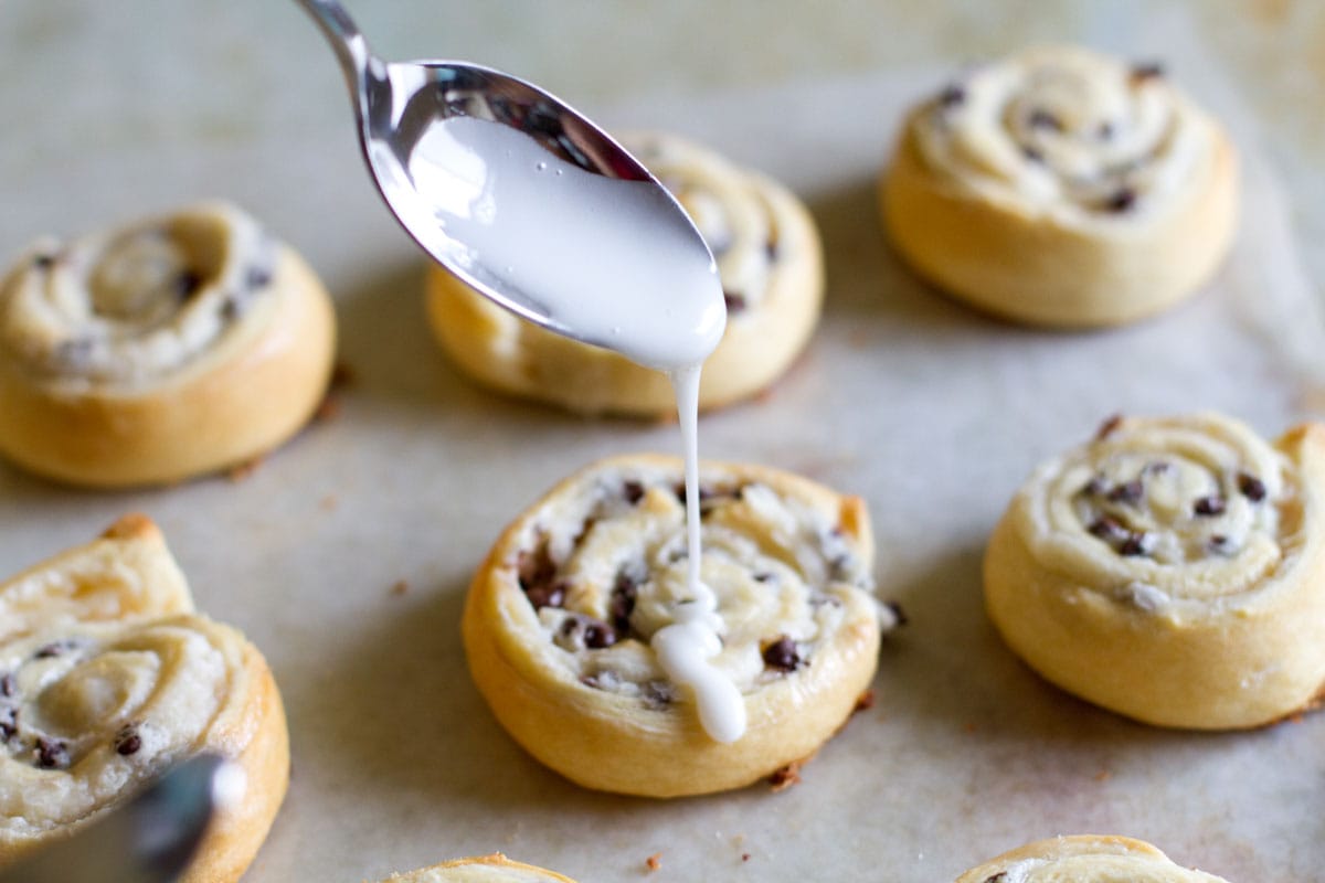 Adding glaze to chocolate chip crescent roll cookies.