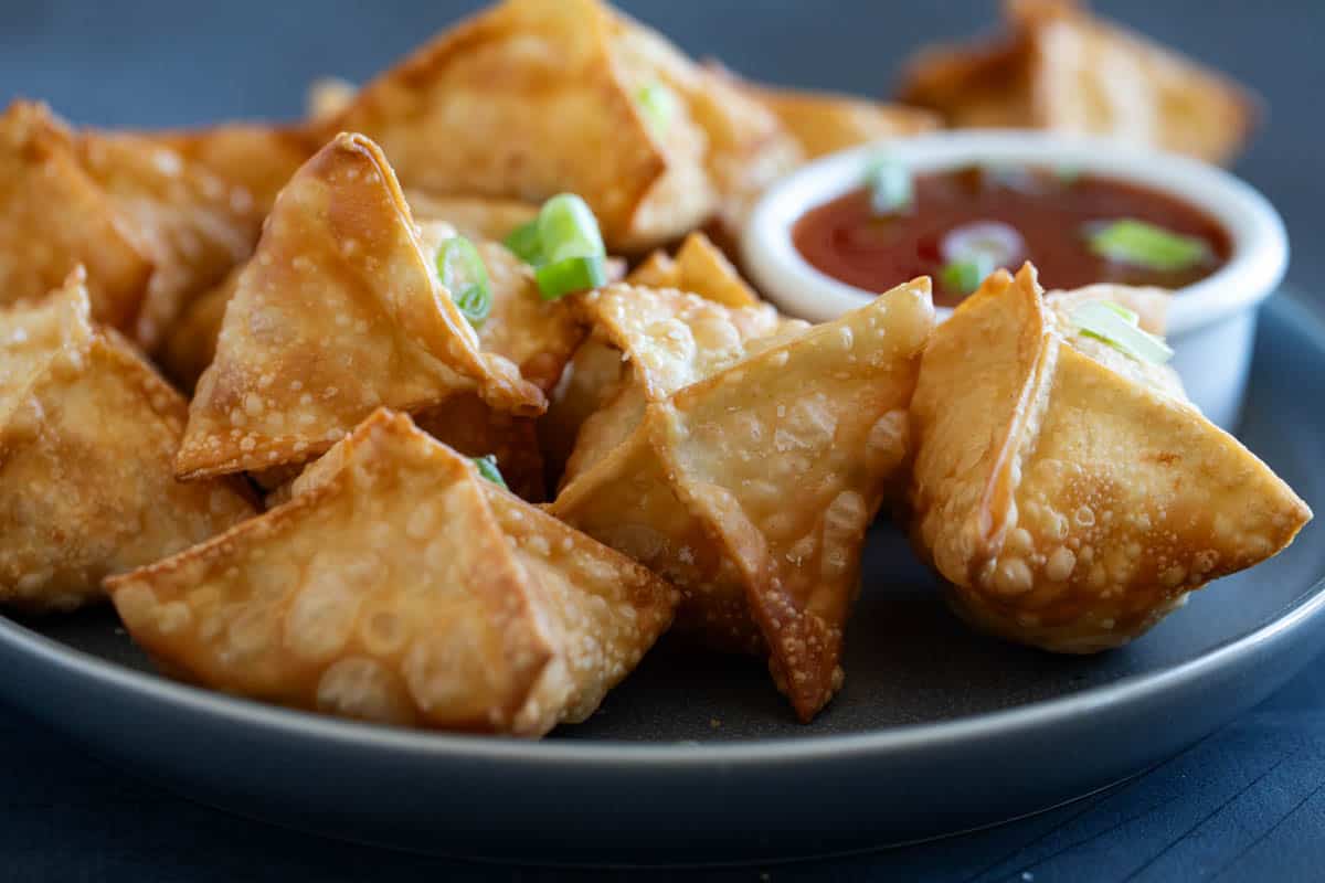 Plate with fried crab rangoon, with bowl of sweet chili sauce for serving.