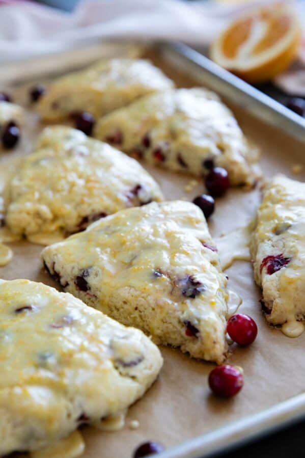 Cranberry orange scones with orange glaze on a baking sheet.