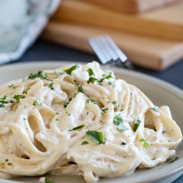 Plate filled with crock pot chicken alfredo topped with greens.