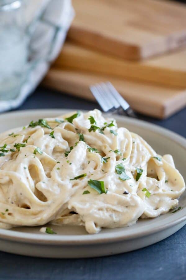 Plate filled with crock pot chicken alfredo topped with greens.