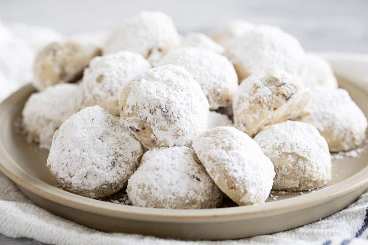 Mexican wedding cookies covered in powdered sugar, on a plate.