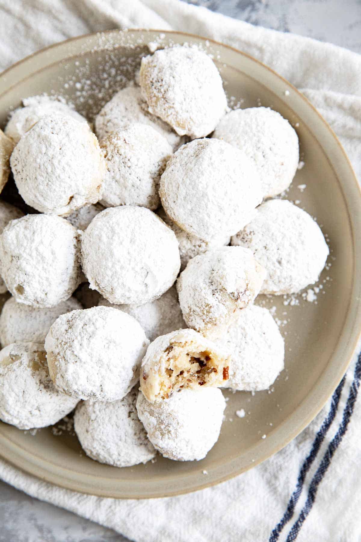 Mexican wedding cookies stacked on a plate, with a bite taken from one cookie.