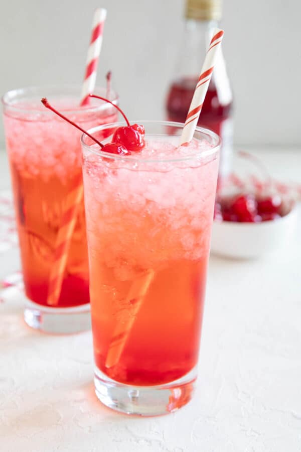 Two glasses filled with Shirley temple mocktail topped with maraschino cherries.