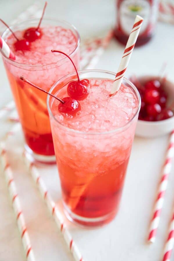 Glasses of Shirley temples topped with maraschino cherries.