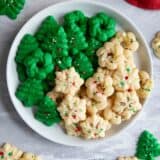 Plain and green Christmas Spritz Cookies on a plate with more cookies around the plate.