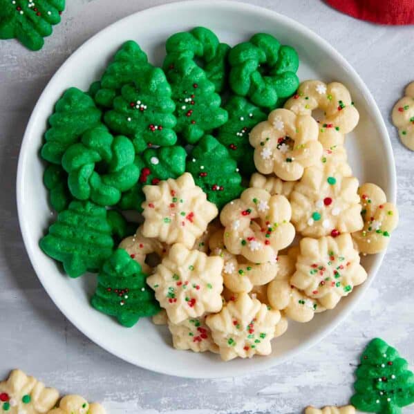 Plain and green Christmas Spritz Cookies on a plate with more cookies around the plate.