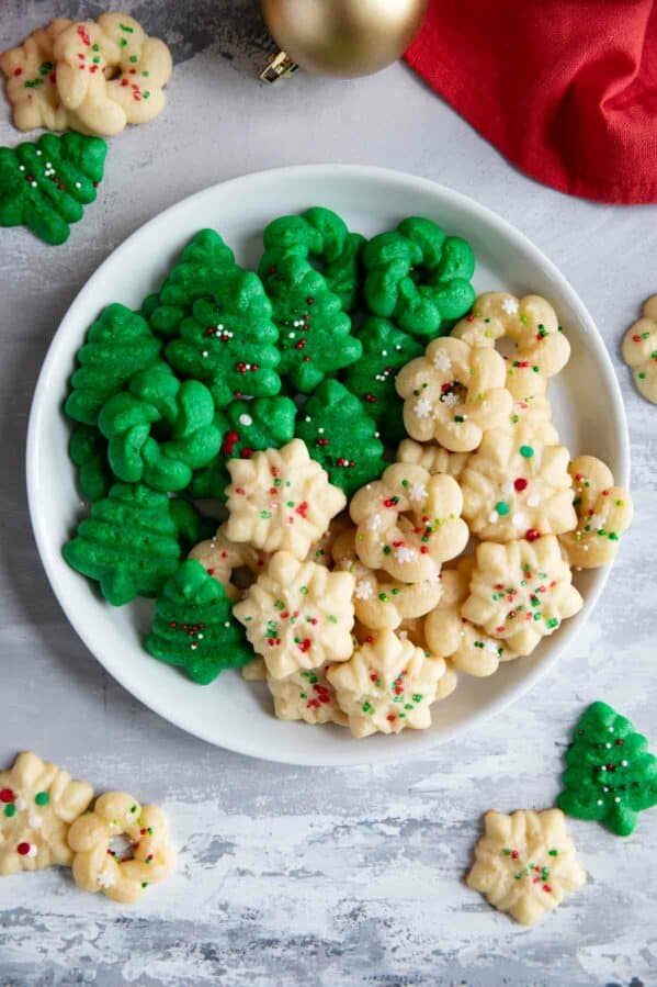 Plain and green Christmas Spritz Cookies on a plate with more cookies around the plate.