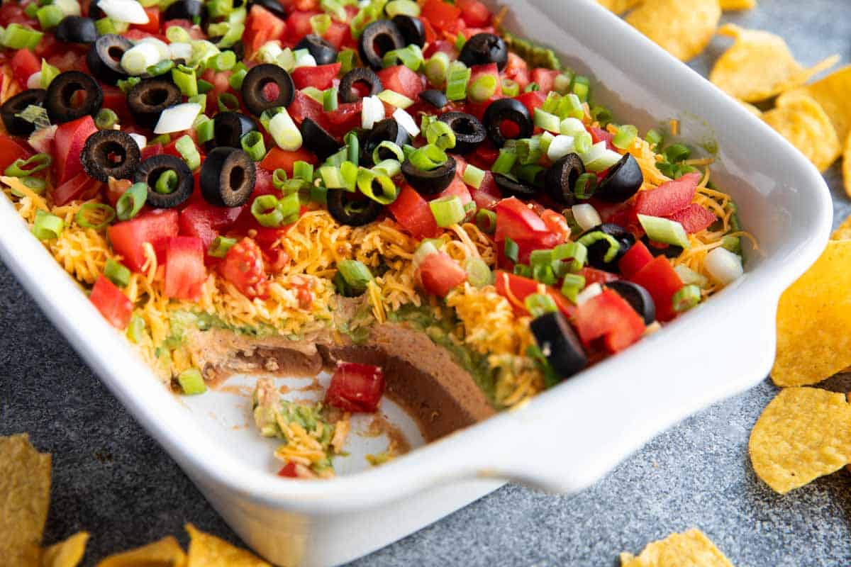 Dish with 7 layer dip, with some of the dip taken from the corner.