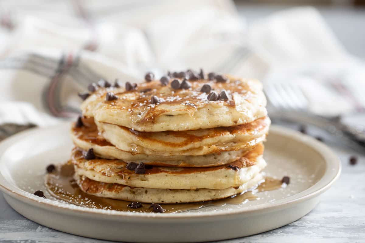 Stack of chocolate chip pancakes with syrup, powdered sugar, and more chocolate chips on top.