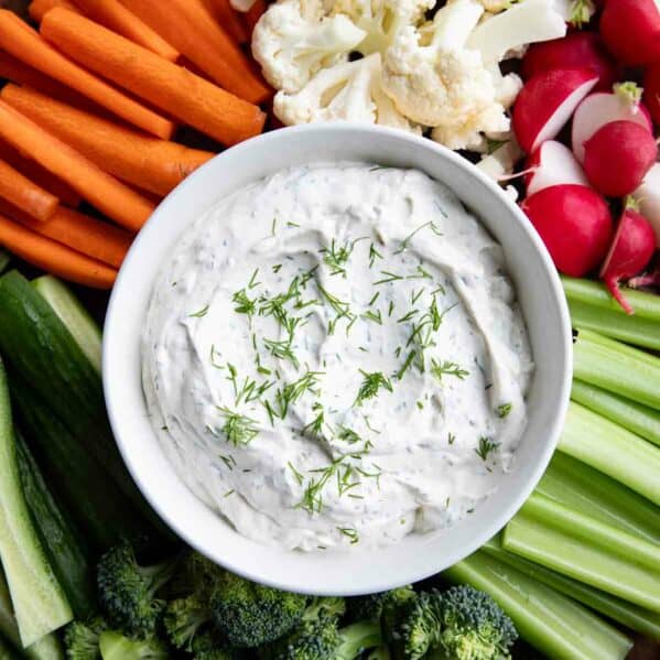 Bowl filled with dill dip, surrounded by assorted vegetables.