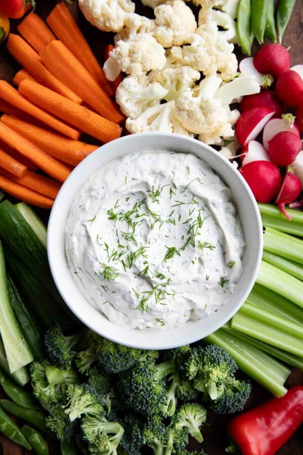 Bowl filled with dill dip, surrounded by assorted vegetables.