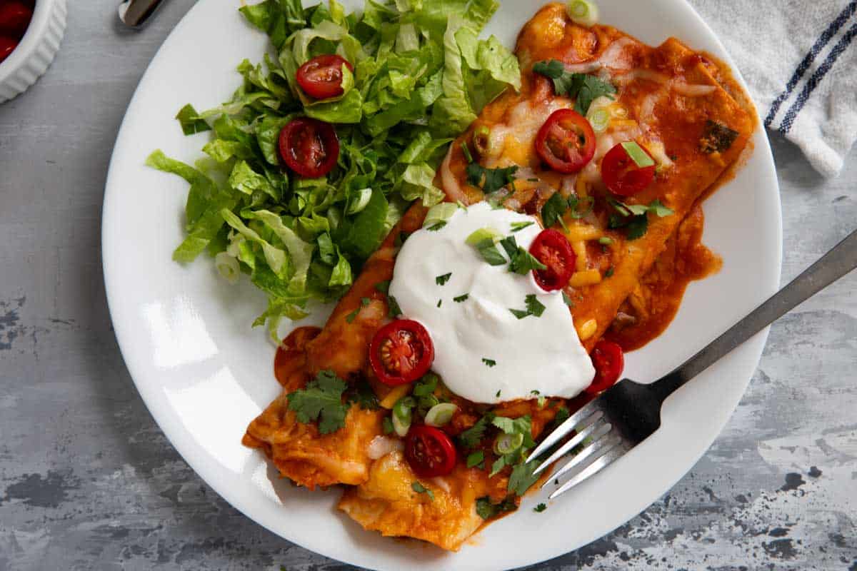 Two ground beef enchiladas with lettuce, tomatoes, and sour cream.