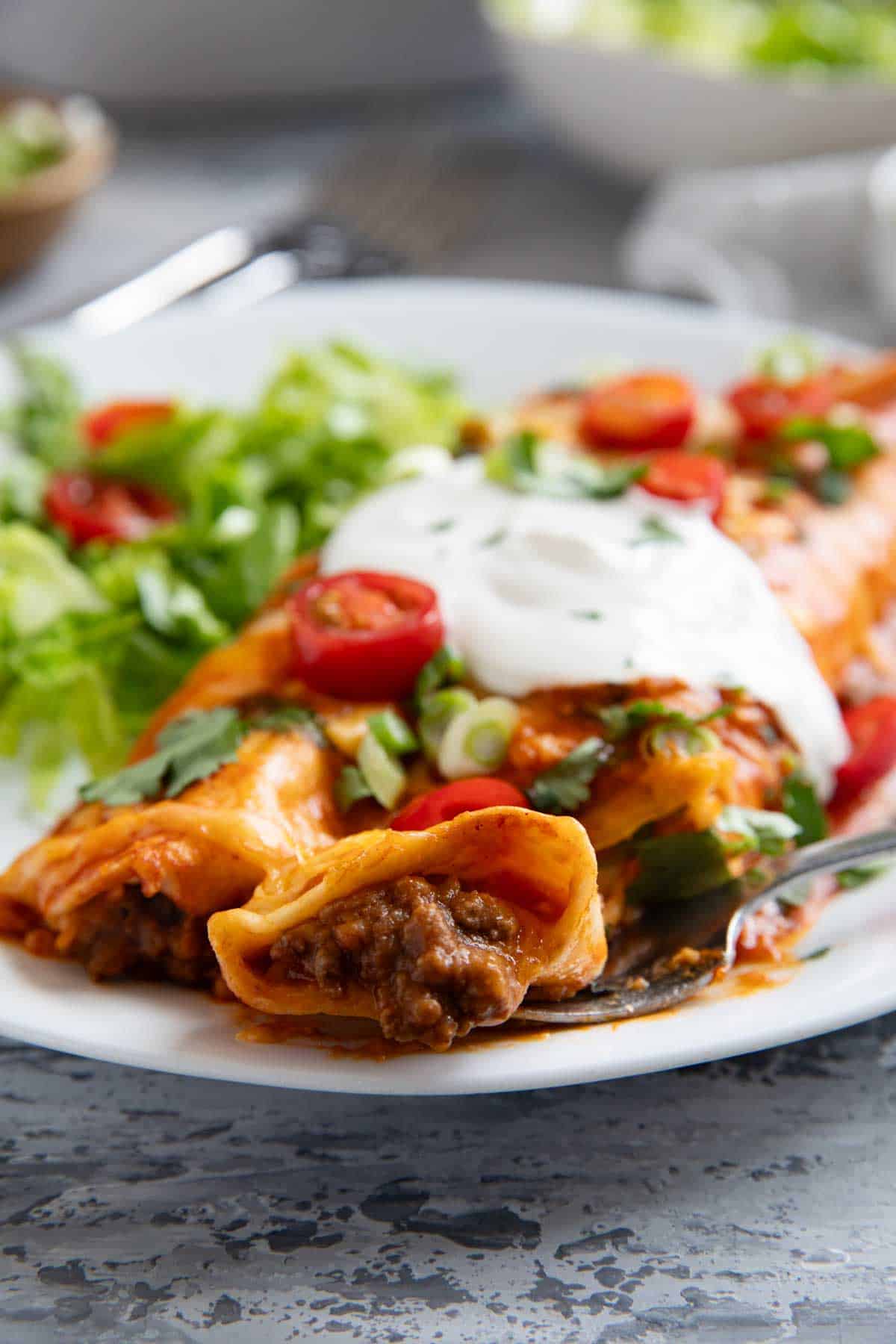 Ground beef enchiladas with a forkful being taken from one enchilada.