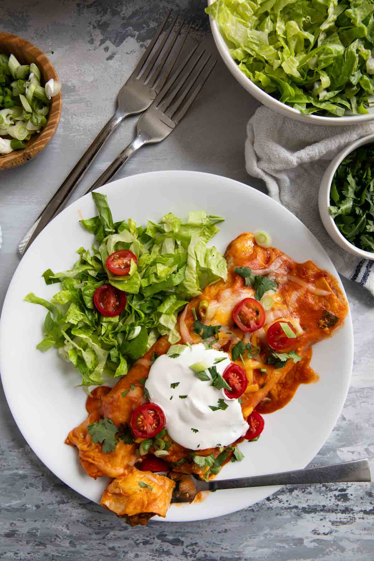 Ground beef enchiladas topped with sour cream tomatoes, and cilantro.