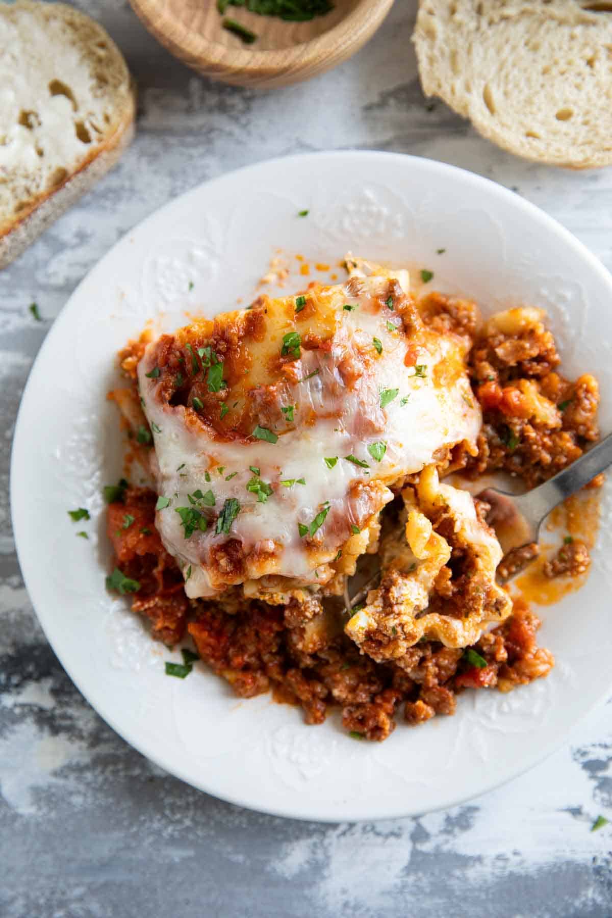 A lasagna roll up on a plate with a bite taken out of it with a fork.