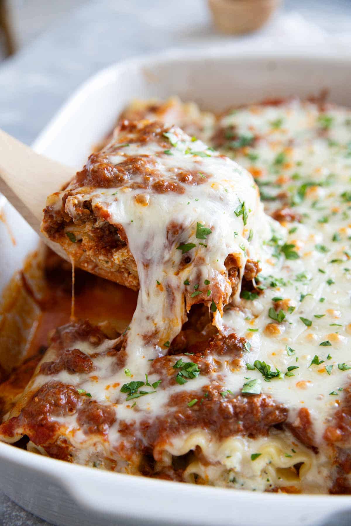 Lasagna Roll Up being removed from a baking dish, with the cheese pulling.