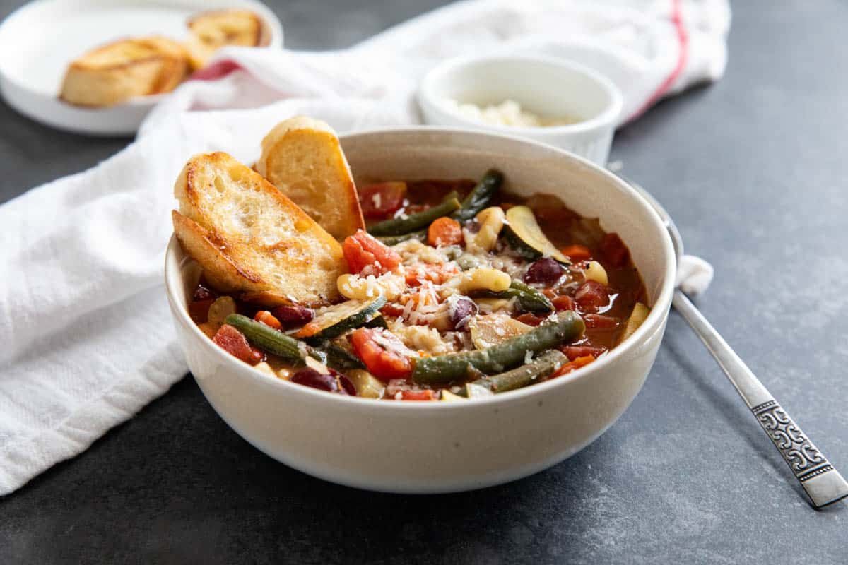 Bowl of Minestrone Soup, topped with parmesan cheese and toasted bread.