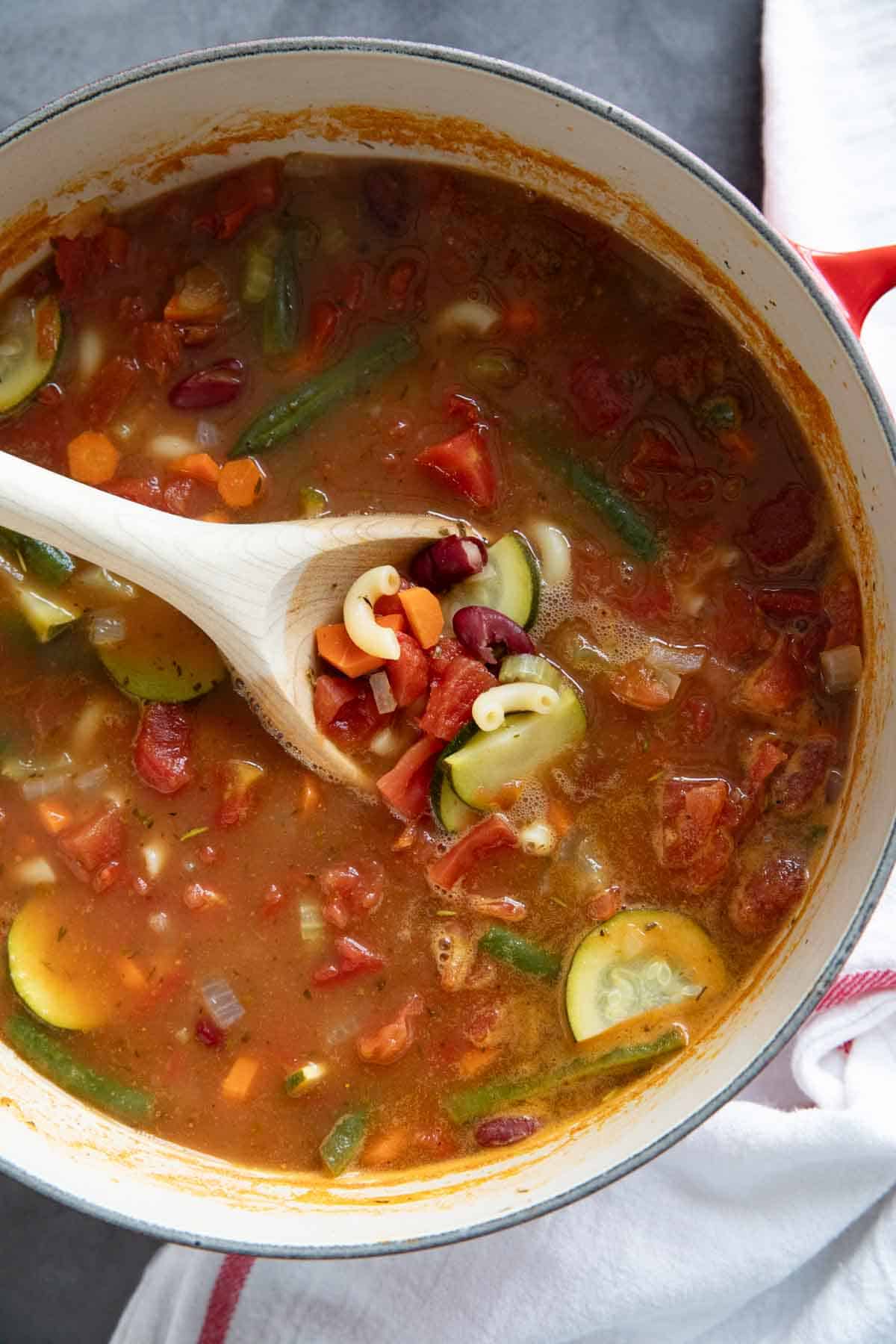 Pot full of Minestrone Soup with a wooden spoon in the soup.