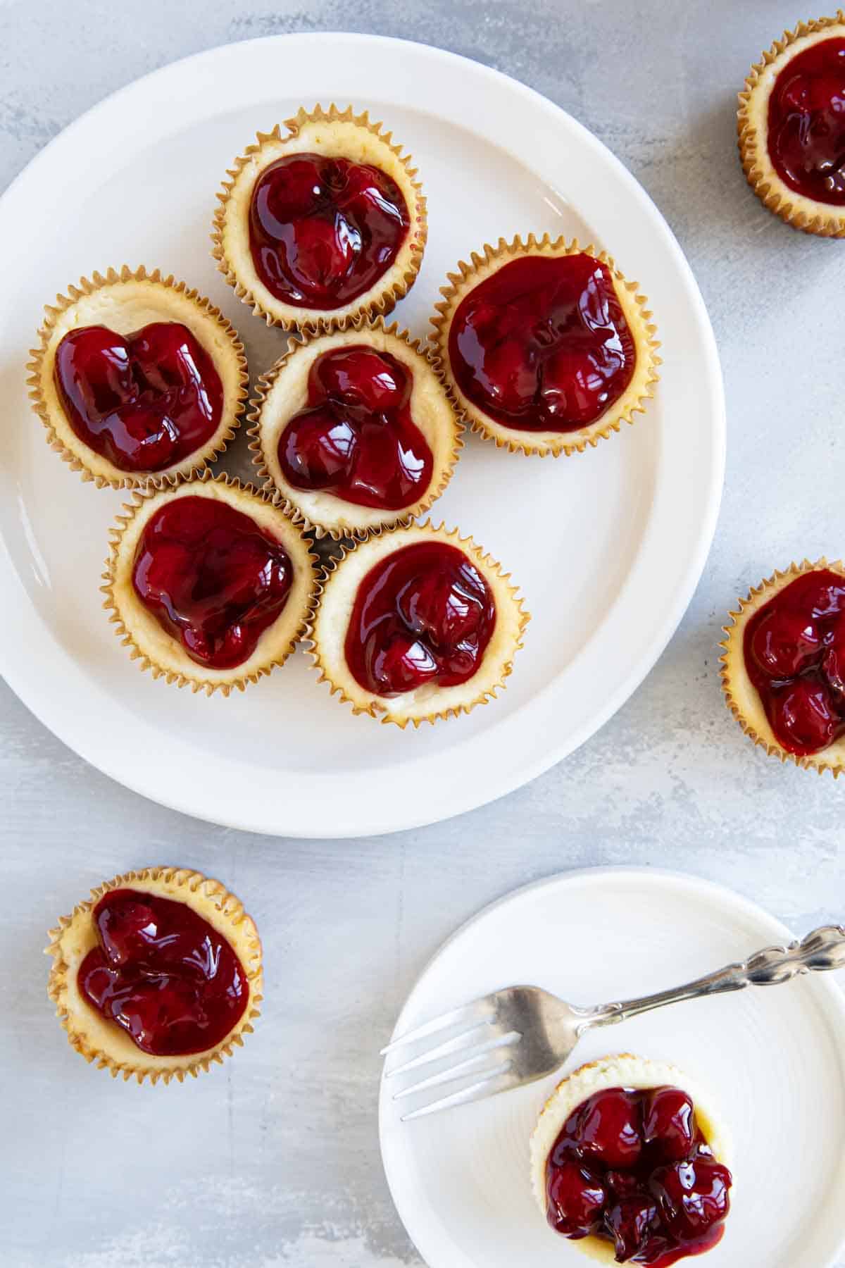 Mini cheesecakes topped with cherry pie filling on plates.