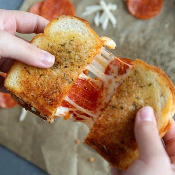 Hands pulling a pizza grilled cheese apart, showing the cheese pull.