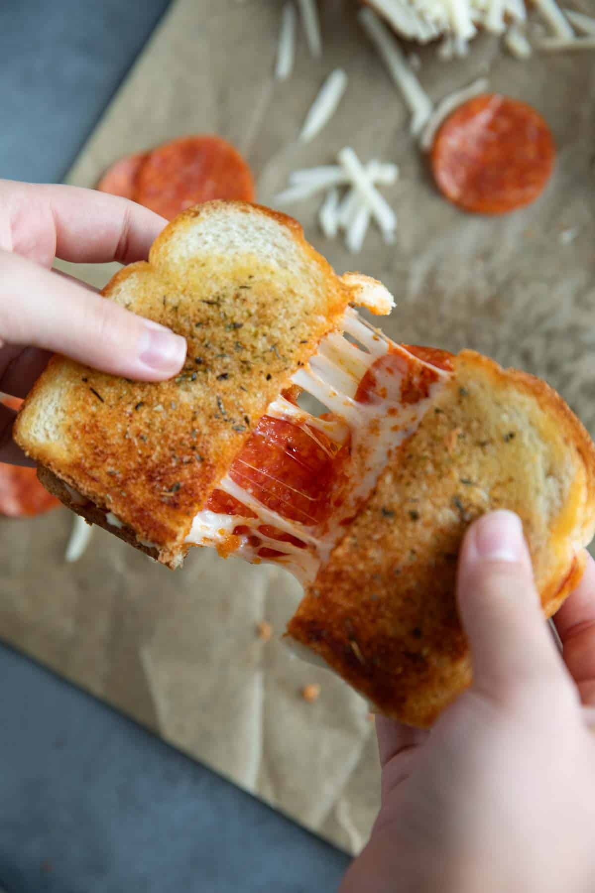 Hands pulling a pizza grilled cheese apart, showing the cheese pull.