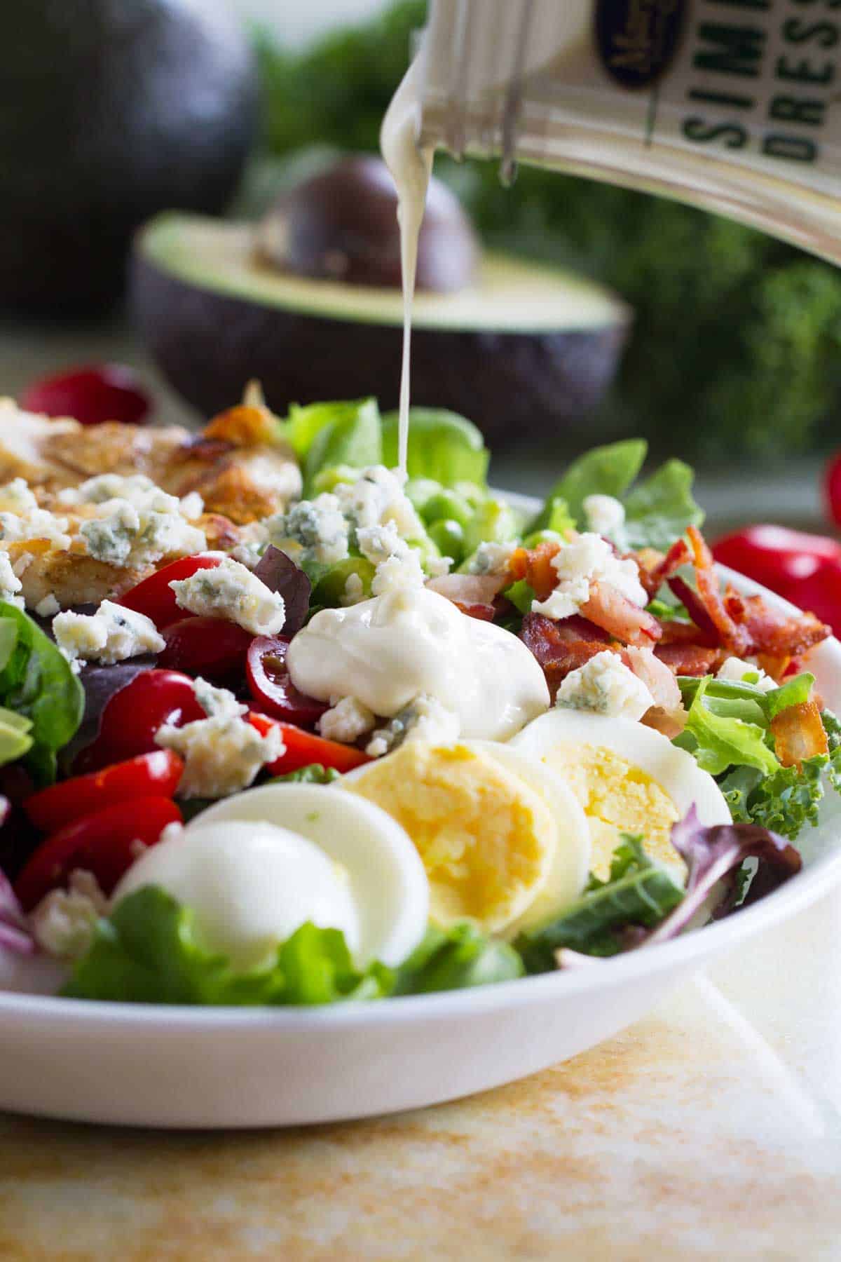 Pouring salad dressing on a Protein Packed Cobb Salad.