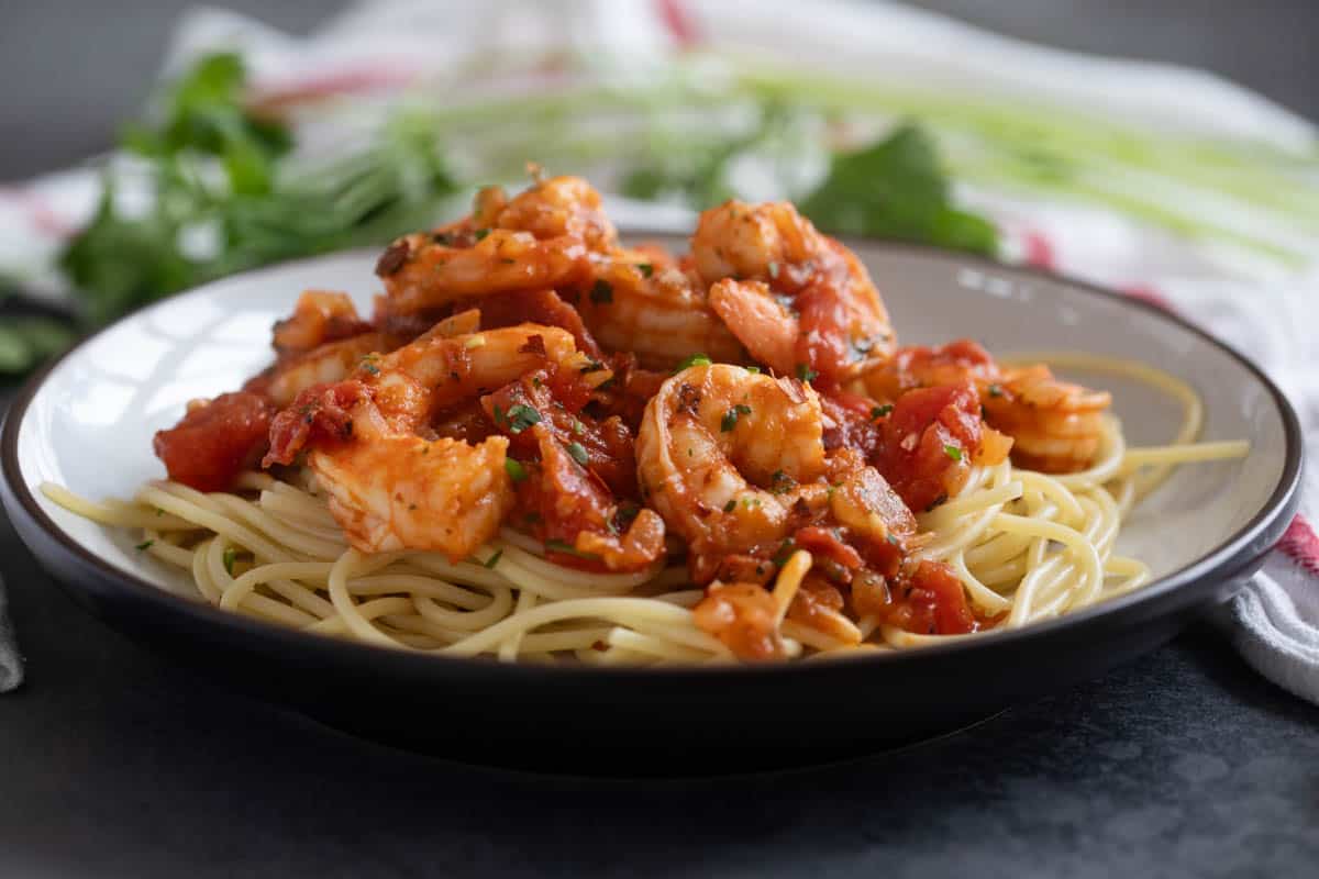 Shallow bowl filled with cooked pasta topped with Shrimp Fra Diavolo.