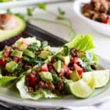 Two taco lettuce wraps on a plate, topped with tomatoes, avocado, and lime juice.