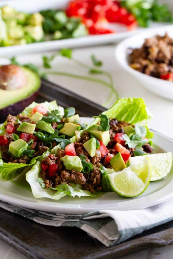 Two taco lettuce wraps on a plate, topped with tomatoes, avocado, and lime juice.