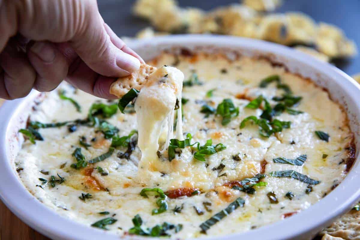 White cheese dip in a dish with a cracker pulling some of the dip out showing cheese pull.