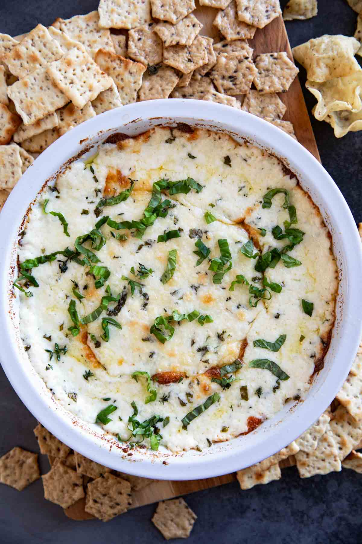 White pie dish filled with white cheese dip, topped with fresh basil.