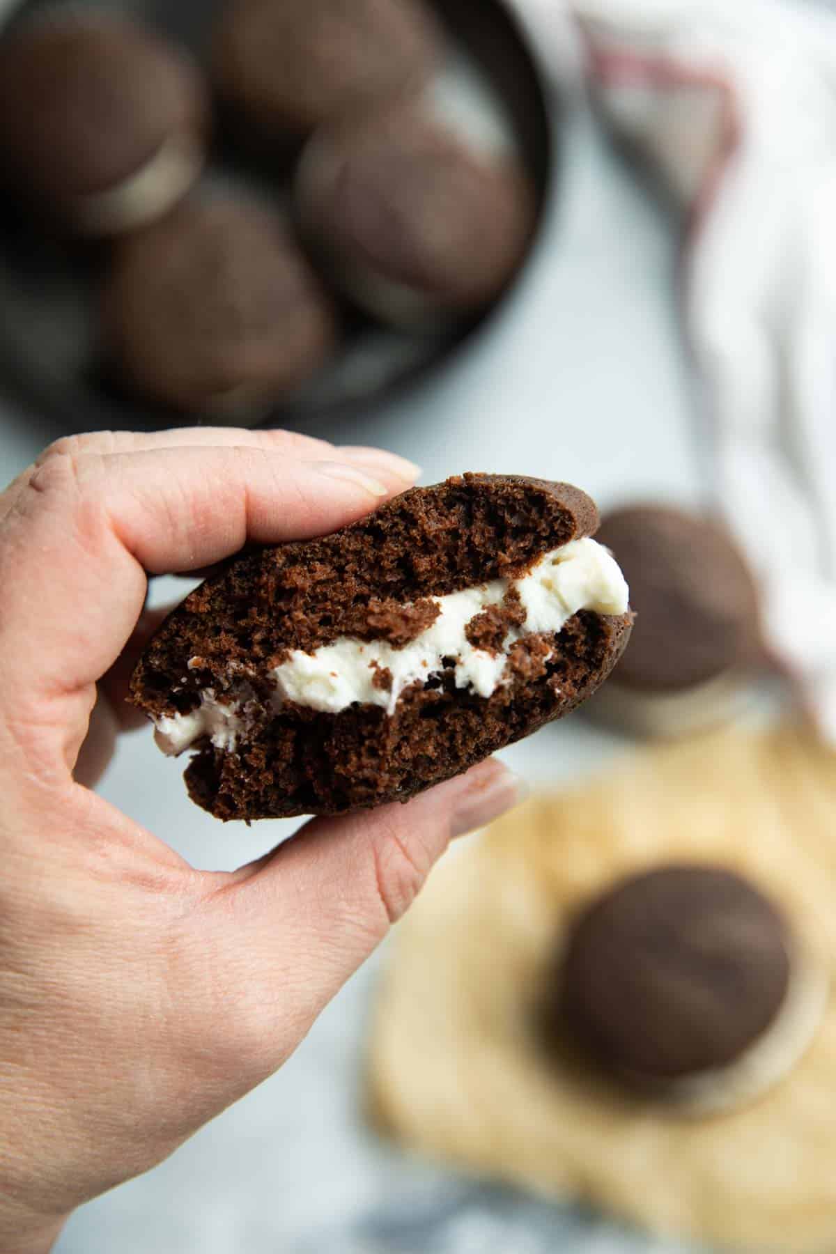 Hand holding a whoopee pie with a bite taken from it.