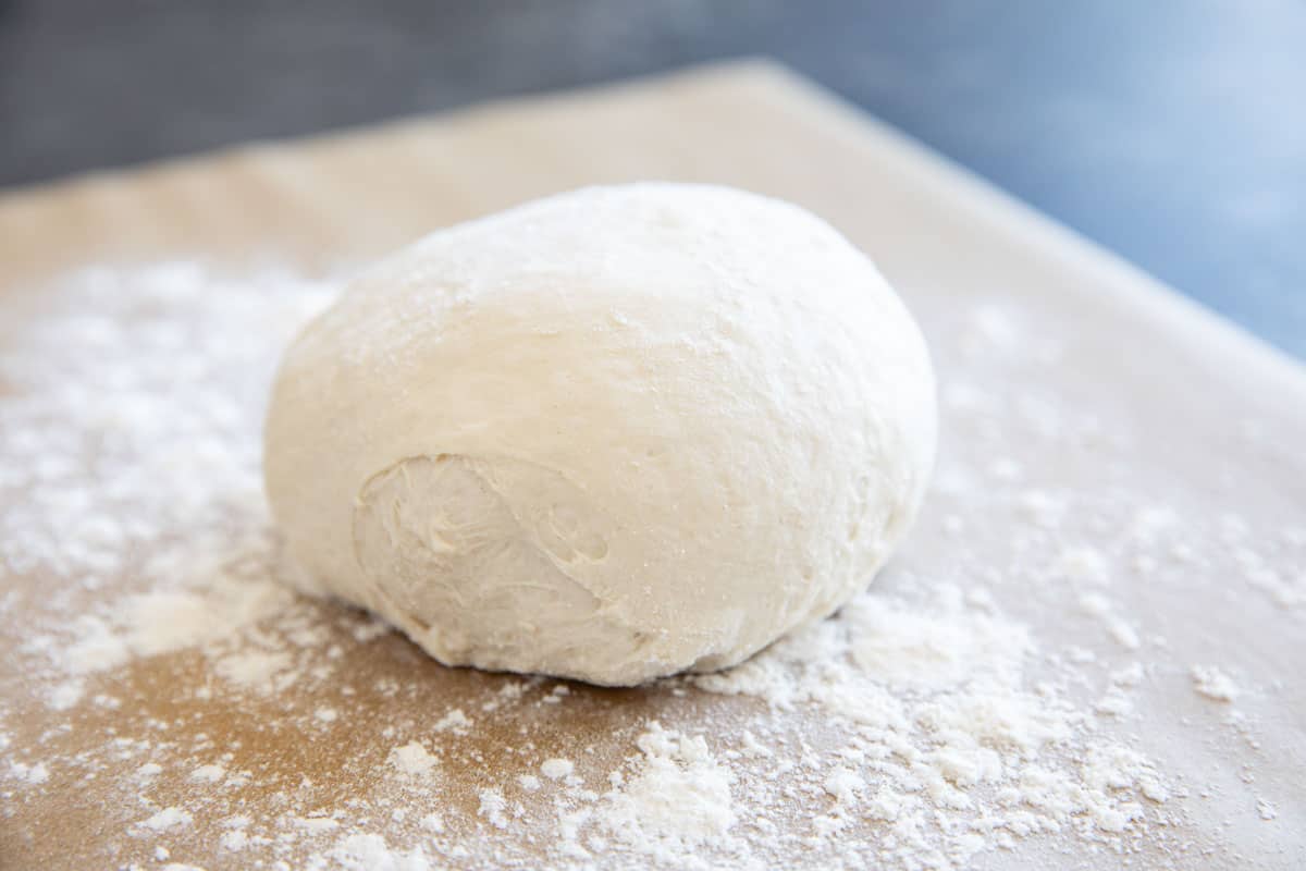 Ball of artisan pizza dough on a piece of parchment paper with flour.