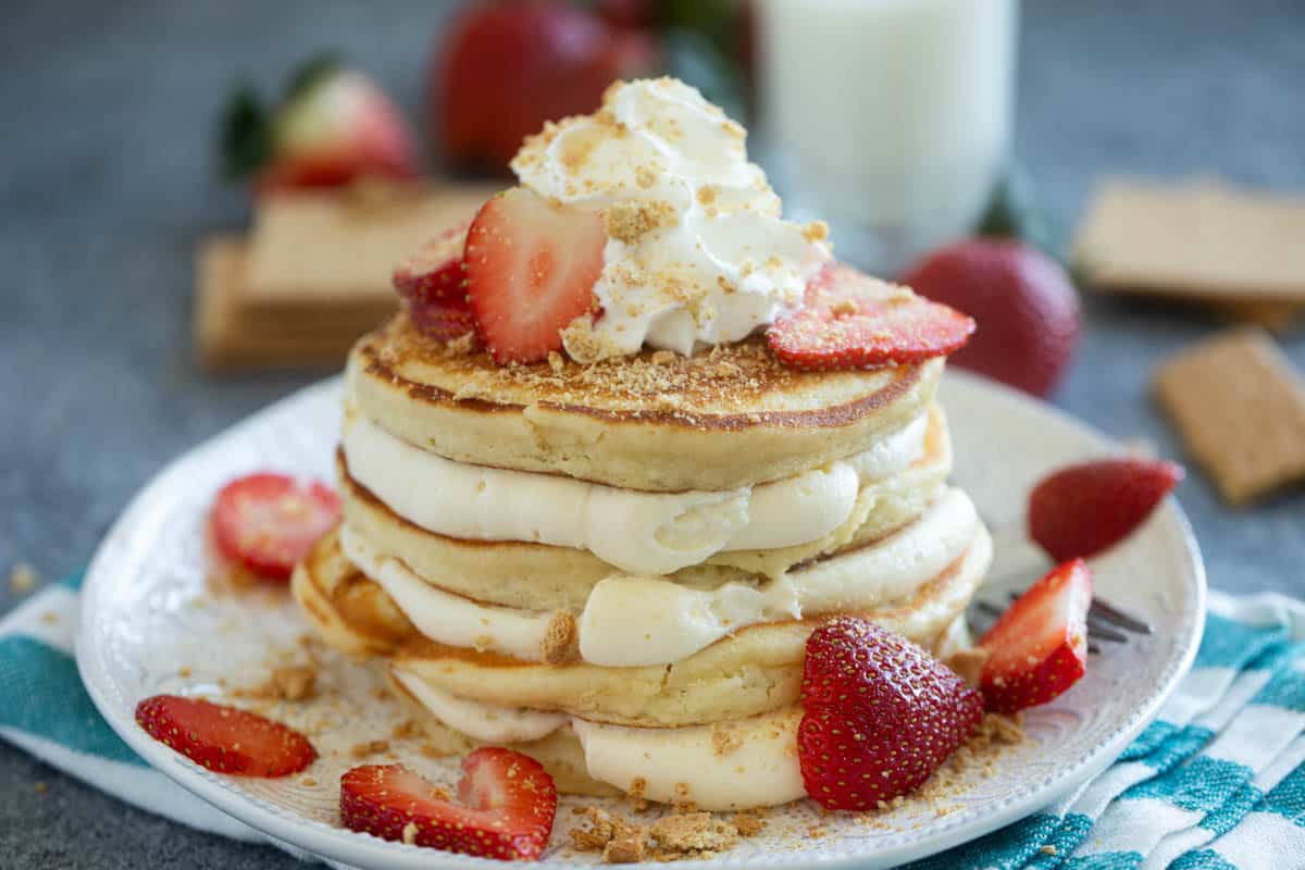 Stack of cheesecake pancakes with cream cheese filling, graham cracker crumbs, and sliced strawberries.