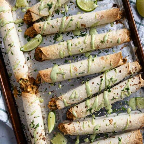 Chicken Flautas drizzled with cilantro ranch on a baking sheet.