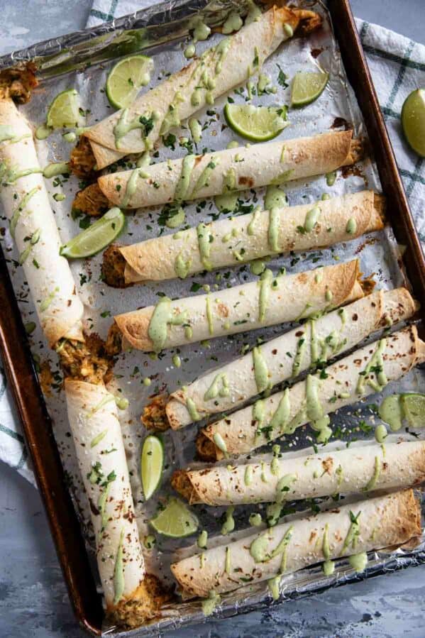 Chicken Flautas drizzled with cilantro ranch on a baking sheet.