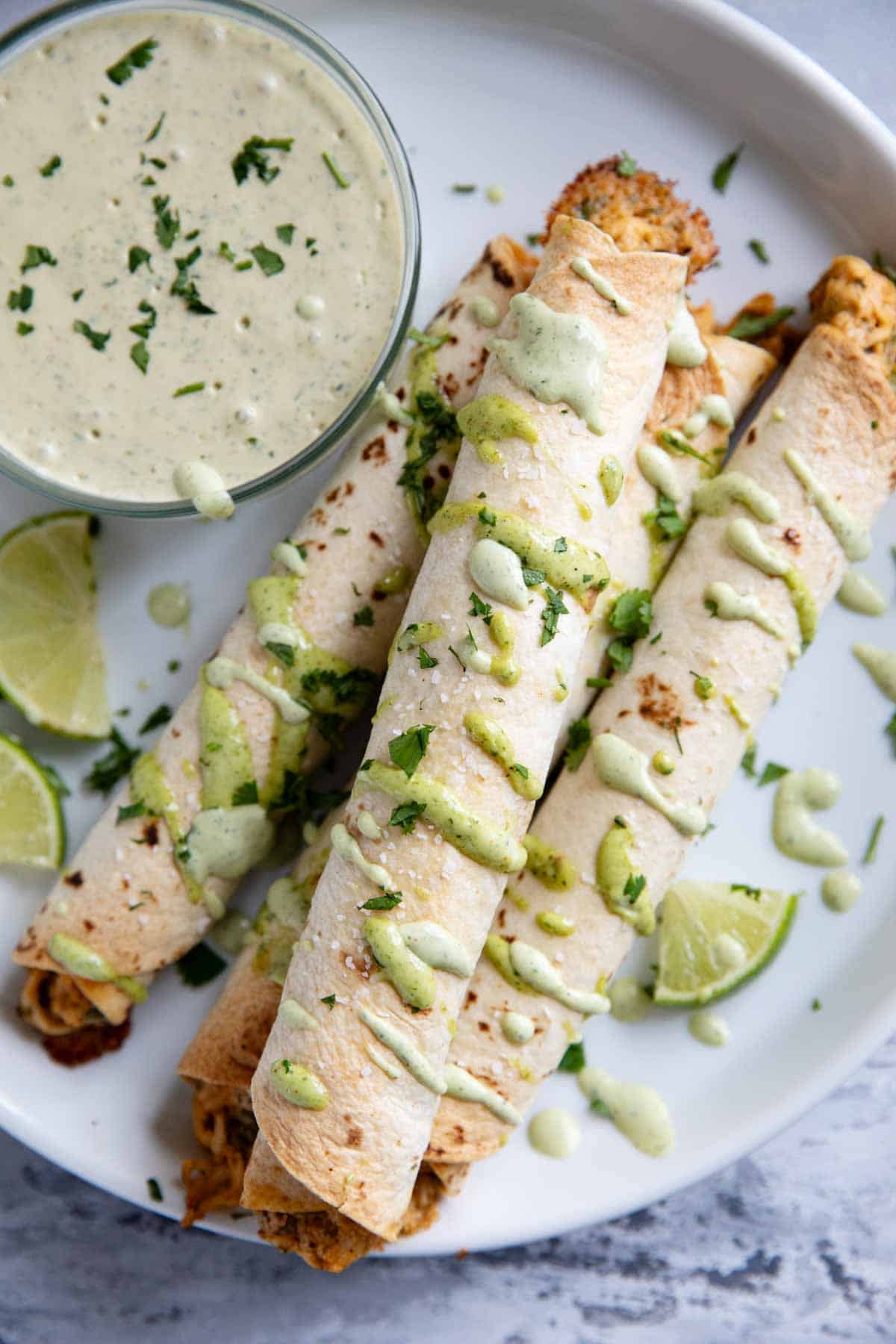 Chicken Flautas on a plate with a bowl of cilantro ranch dipping sauce.