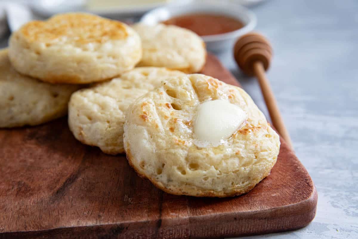 Crumpets on a cutting board, with butter on top of one crumpet.