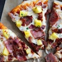 Slice of Hawaiian pizza topped with ham, bacon, and pineapple.