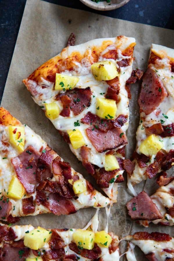 Slice of Hawaiian pizza topped with ham, bacon, and pineapple.