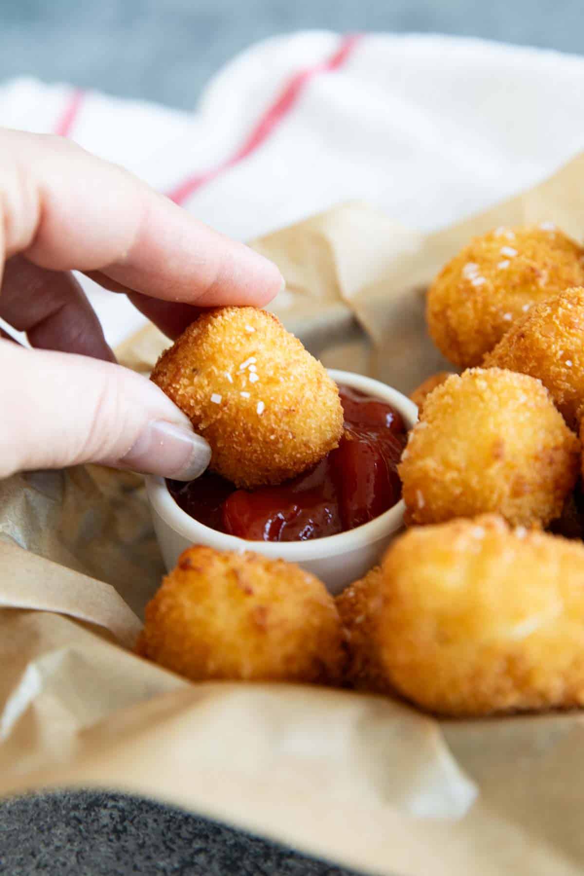 Hand dipping a homemade tater tot into ketchup.